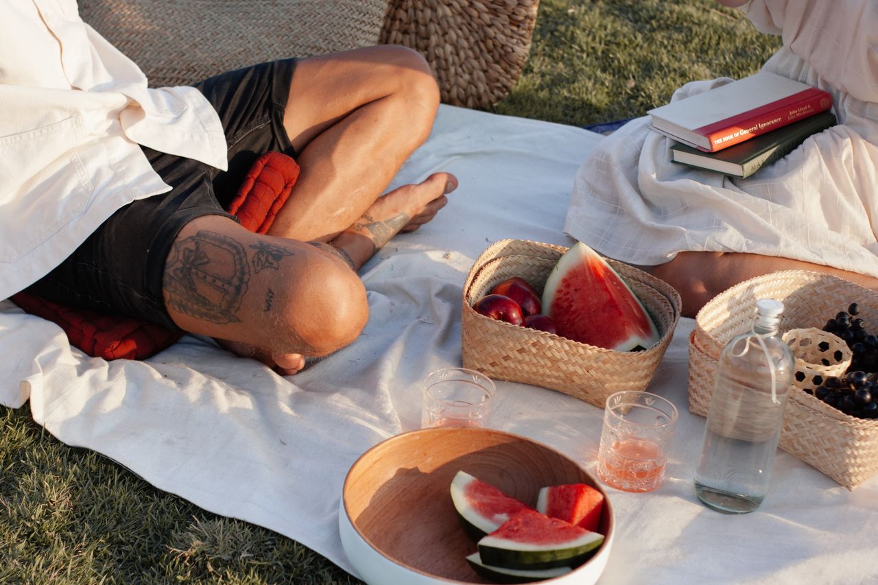 A cozy outdoor picnic with watermelon, books, and drinks on a sunny day.